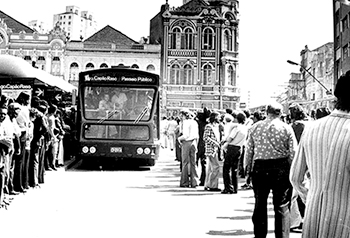 Foto histórica traz imagem frontal de um ônibus aguardado por uma grande fila de passageiros.