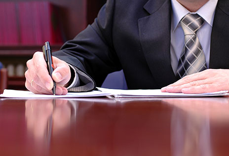 imagem retrata advogado de terno e gravata escrevendo em mesa de escritório em imagem fechada ocultando o rosto
