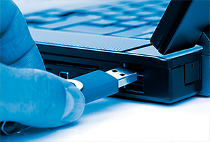 Imagem em corte e plano fechado mostra uma pessoa conectando um pendrive em laptop.