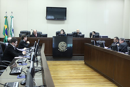 Vista geral do plenário onde se realizou a audiência, tendo ao fundo a mesa da presidência e, em primeiro plano, as partes em suas bancadas