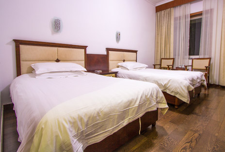 imagem mostra um quarto duplo de hotel, com duas camas de solteiro arrumadas paralelamente, vistas em perspectiva