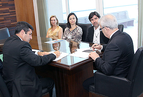 Imagem em plano médio mostra o desembargador Altino Pedrozo dos Santos e o secretário do TCU, Luiz Andriolli, assinando termo de cooperação. Na mesa é possível também três servidores do TRT-PR que participaram da reunião.