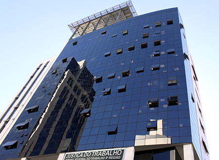 Imagem em plano geral mostra fachada da sede do TRT-PR. A imagem foi produzida a partir da calçada frontal do edifício, de baixo para cima, mostrando o prédio em perspectiva.