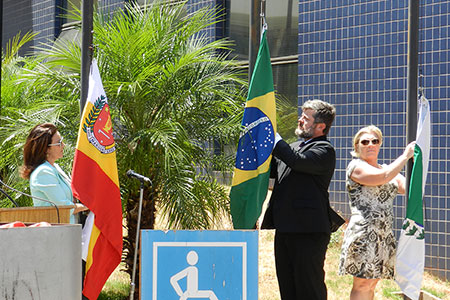 imagem mostra o juiz Marcus aurelio Lopes ao centro  hasteando a bandeira nacional, enquanto servidores ao seu lado hastiam as bandeiras de Maringá e do Paraná