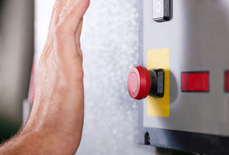 imagem mostra uma mão se aproximando para acionar botão de emergência para desligar máquina