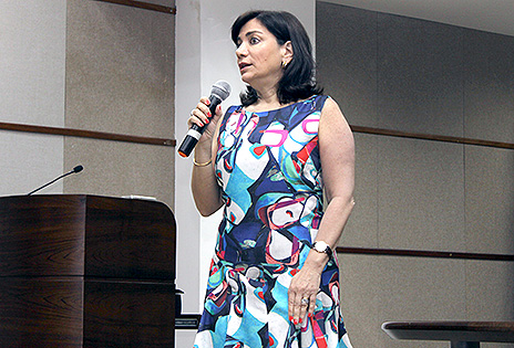 Imagem em plano médio mostra a médica Keti Styliano Patsis dirigindo-se ao público presente no evento. A palestrante está com um microfone sem fio na mão.