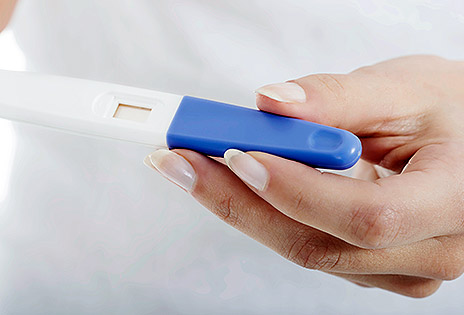 Imagem em plano detalhe mostra mão feminina segurando dispositivo utilizado para realizar teste de gravidez