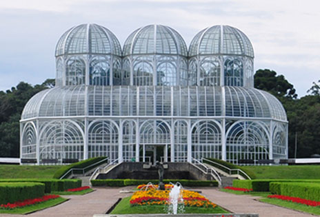 imagem mostra a estufa do Jardim Botânico de Curitiba com partes dos jardins em primeiro plano