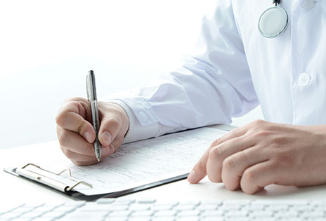 imagem ilustrativa mostra em plano fechado as mão de um médico preenchendo a caneta um documento