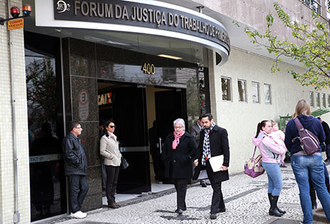 A foto, em plano geral, mostra a fachada do Fórum da Justiça do Trabalho e algumas pessoas que transitam pela calçada.