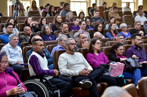 Foto da plateia que acompanhava os denates. Aparecem sete fileiras de poltronas, lotadas, e no primeiro plano está um participante em cadeira de rodas.