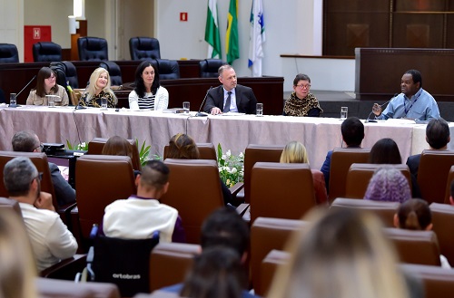 à mesa de honra, o desembargador Baracat e quatro mulheres ouvem o servidor Jorge Pires, do arquivo do TRT, na extremidade direita da mesa. Na extremidade oposta, estão Maria Gabriela Gimenez da Silva Mendonça, a Gabi, jovem com síndrome de down.