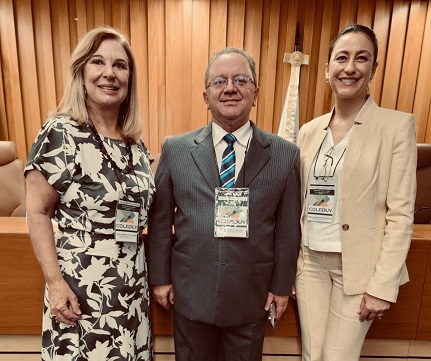 Fotografia com três pessoas, com imagem da altura dos joelhos até a cabeça. À esquerda, Antonia Regina Tancini Pestana, desembargadora Ouvidora do TRT15 e Presidente do Colégio de Ouvidores da Justiça do Trabalho - Coleouv; mulher de pele branca, cabelos loiros e usa vestido florido. No centro, o vice ouvidor do TRT-PR, desembargador Edmilson Antonio de Lima, homem de pele branca, cabelos loiros, usa óculos e veste terno cinza, camisa branca e gravata em tons de azul. À direita, Débora Proença, gestora da Ouvidoria do TRT-PR< mulher de pele bramca, cabelos escurtos presos, ela usa calça e blazer bege com camisa branca. 