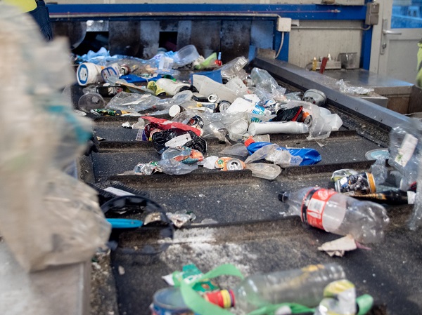 Fotografia de uma esteira mecânica com transporte de lixo - garrafas plásticas, latas e pedaços de plástico. 