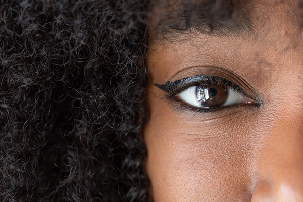 Fotografia mostra parcialmente o rosto de uma mulher negra, de olhos castanhos e delineador. Enquadramento mostra parte do lado direito do rosto, metade do nariz, bochechas, olho direito e o cabelo crespo.
