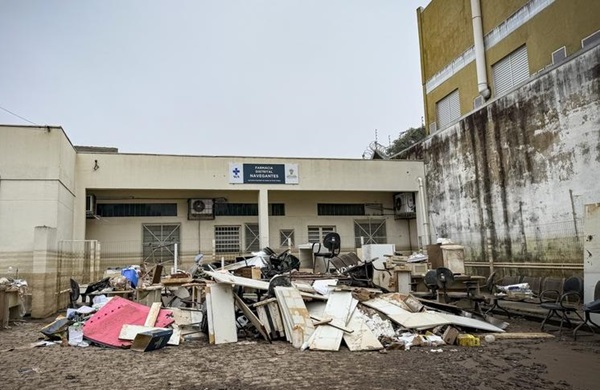 Fotografia da fachada do Centro de Saúde Navegantes com as paredes sujas de barro e lama a mais de um metro do chão. Em frente ao prédio, entulhos de móveis e utensílios estragados pela enchente.