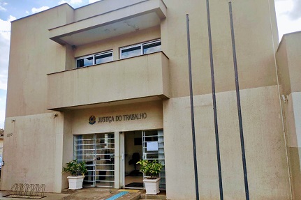 Fotografia da fachada de um prédio cor bege escuro com dois andares. Sobre a porta de entrada, no térreo, o brasão da República e escrito: Justiça do Trabalho.