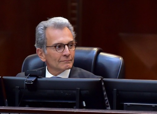 Fotografia do ministro Alexandre Ramos sentado em uma cadeira de couro em frente a uma mesa de madeira com telas de computador à frente. Ministro é um homem branco, de gabelos curtos grisalhos e usa óculos.