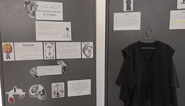 Painel sobre o Dia da Juíza e do Juiz do Trabalho (26 de abril) com desenhos (cérebro, coração, mãos, balança, caveira), textos e uma toga pendurada ao lado.