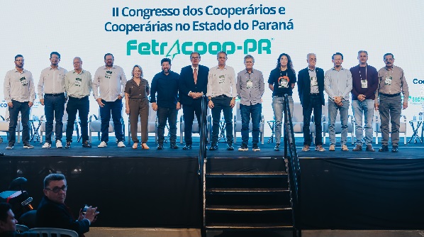 Foto de 14 pessoas pessoas perfiladas lado a lado em um palco. Atrás telão escrito: II Congresso dos Cooperários e Cooperárias do Estado do Paraná
