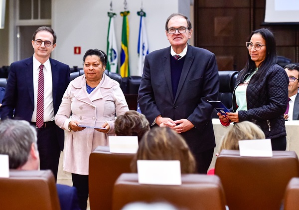 Fotografia de dois homens de terno e duas mulheres segurando a cartilha do trabalhador latinoamericano em frente a uma plateia.