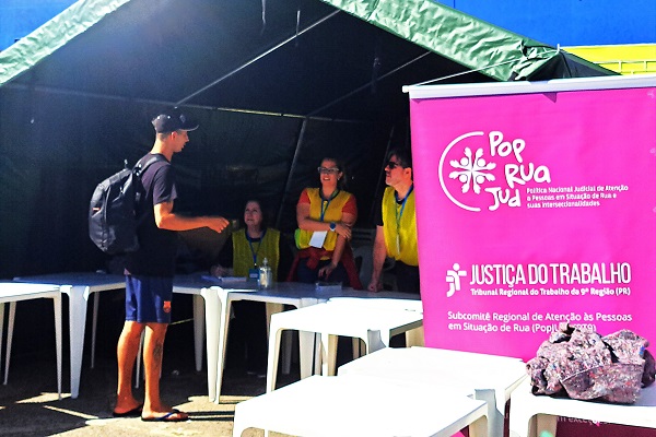 Um homem recebe donativos em frente ao stand do TRT-PR no PopRuaJud 2025