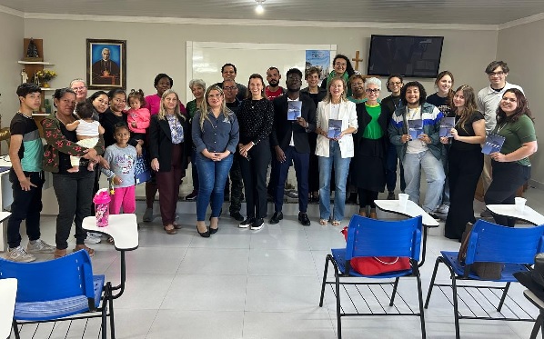 Fotografia de 28 pessoas agrupadas e perfiladas, lado a lado, dentro de uma sala de aula, com carteiras azusi na frente do grupo