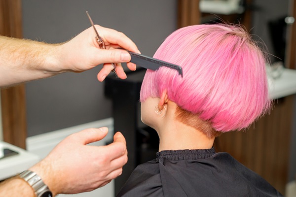 Mãos de cabeleireiro penteando cabelo rosa curto para uma pessoa de costas em um salão de beleza