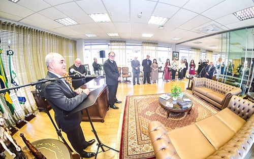 Fotografia com lente grande angular, que distorce as bordas para ampliar a área, mostra ministro Brandão em primeiro plano falando em tribuna e grupo de cerca de 15 pessoas em pé ouvindo