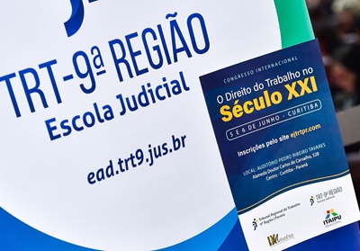 Fotografia de um banner e um folder com a logomarca da Escola Judicial do TRT9 e um folder sobre o evento