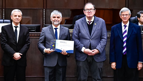 Fotografia de quatro homens brancos de terno em p&eacute;, perfilados lado a lado. O segundo, juiz Braulio, segura trofeu e certificado