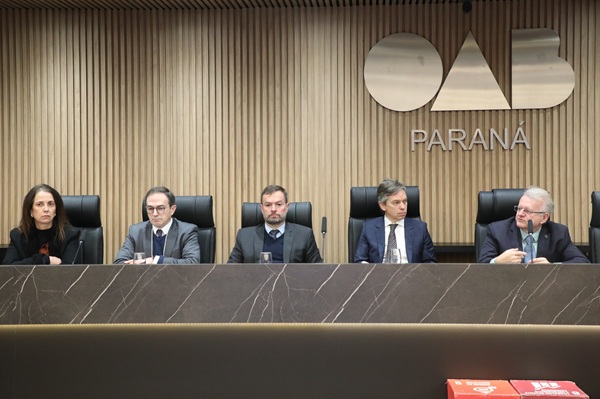 Fotografia de cinco pessoas sentadas em cadeiras de couro em frente a mesa de m&aacute;rmore, s&atilde;o quatro homens e uma mulher. 