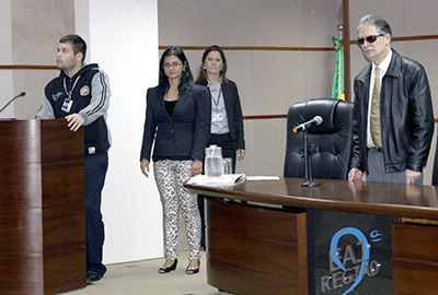 Imagem em plano geral mostra em primeiro plano o desembargador Ricardo Tadeu Marques da Fonseca, de pé, por detrás da mesa do auditório da Escola Judicial, durante evento de entrega de certificados do curso de Libras para servidores do TRT-PR. Na imagem aparecem outros servidores do tribunal e, ao fundo, é possível ver a bandeira do Brasil, num canto da sala.