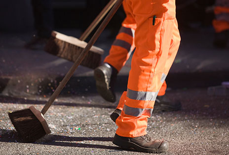 imagem fechada em que aparecem pernas de varredores de rua e suas vassouras enquanto trabalham