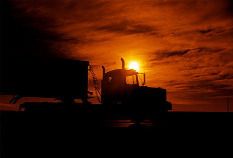 imagem mostra silhueta de caminhao passando por rodovia com o sol de pondo por detrás da cabine do veículo