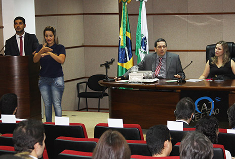 Imagem mostra do lado direito a mesa com o procurador Sergio Caribé e a servidora do TRT-SP Daniela Kovács. Do lado esquerdo da imagem, tradutora de libras informa à plateia o que a servidora Daniela fala. Na parte inferior direita da imagem vê-se o desembargador Ricardo Tadeu Marques de fones de ouvido, com acesso à audiodescrição de imagens.