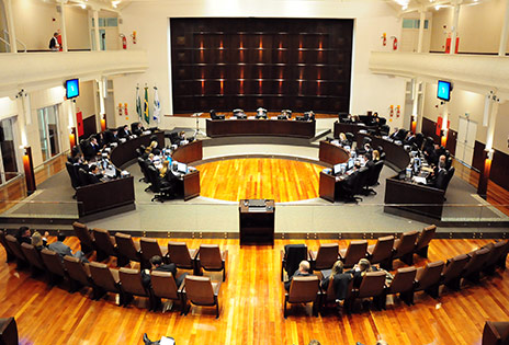 A foto, tirada de cima, em plano geral, mostra todo o Tribunal Pleno. Na parte inferior da foto, &eacute; poss&iacute;vel ver algumas cadeiras da plateia e, no centro da foto, as bancadas do pleno, ocupadas pelos desembargadores.